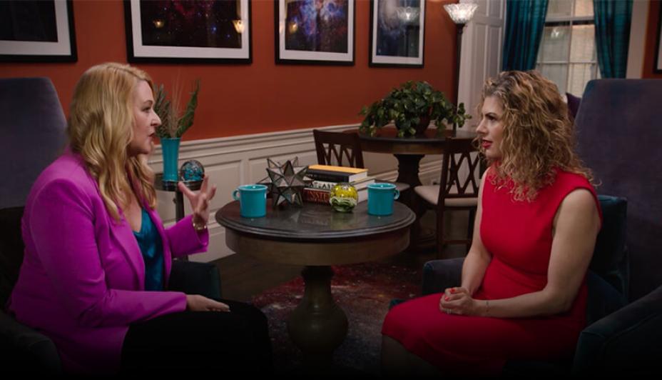 Two women sitting together in a red room conducting an interview.